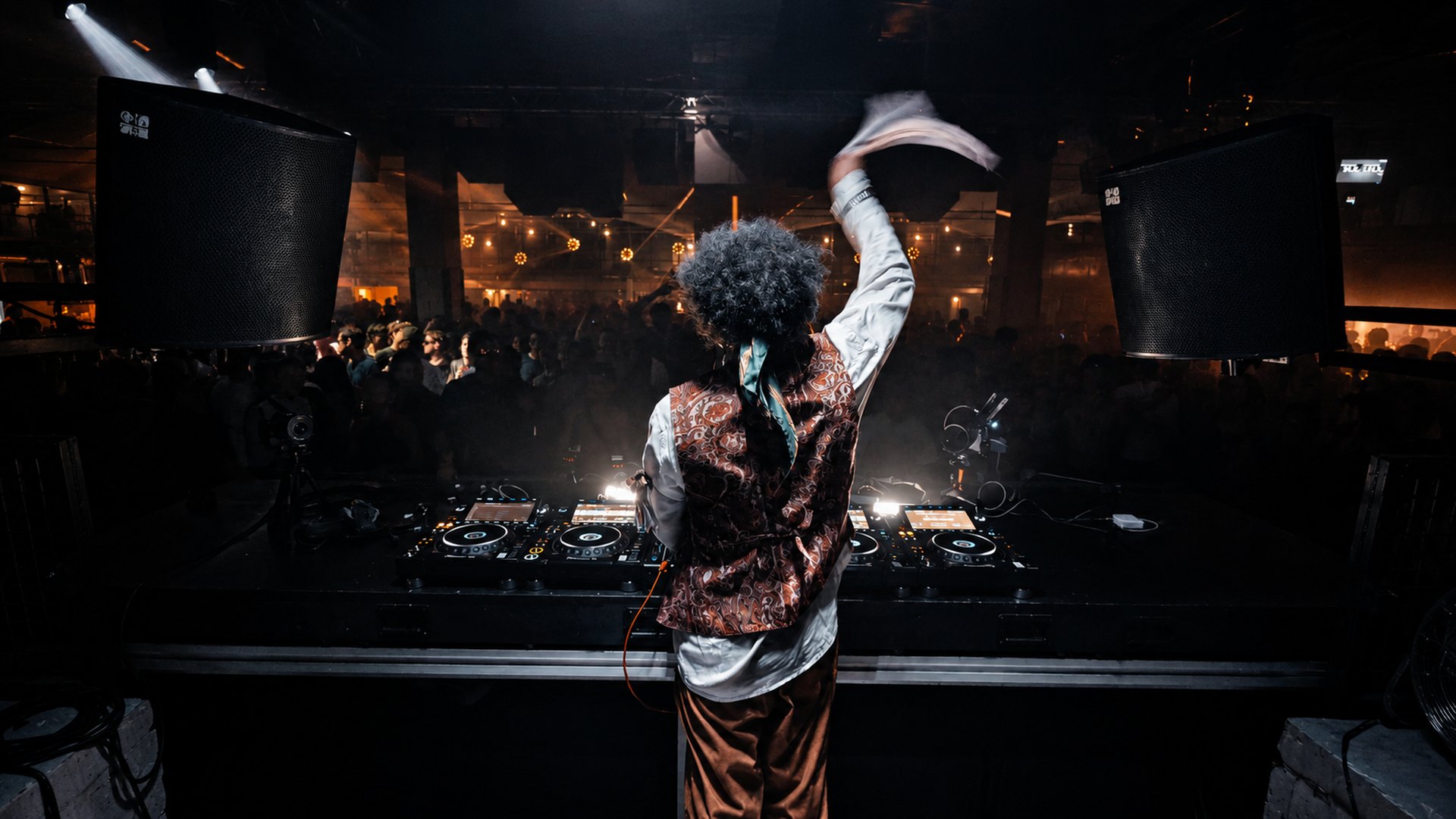 BabaBass3000 behind the decks, arms raised in front of a packed crowd